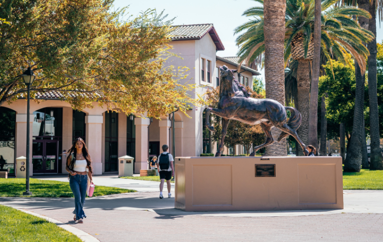 A male student and a female student walking past the large bronco statue