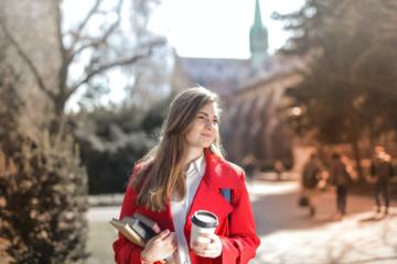 Student on a university campus with a coffee in one hand and books in another 