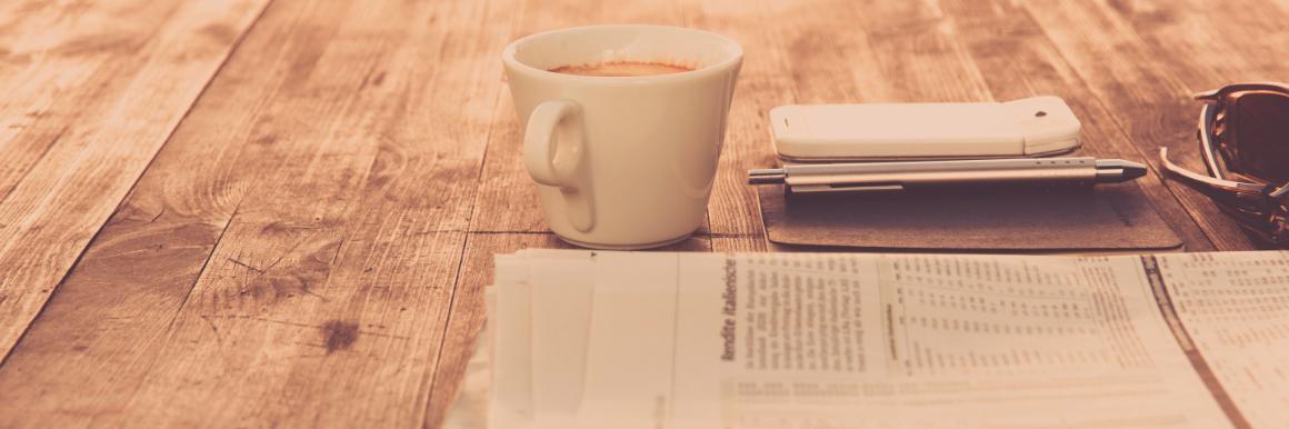 Newspaper next to phone and cup of coffee