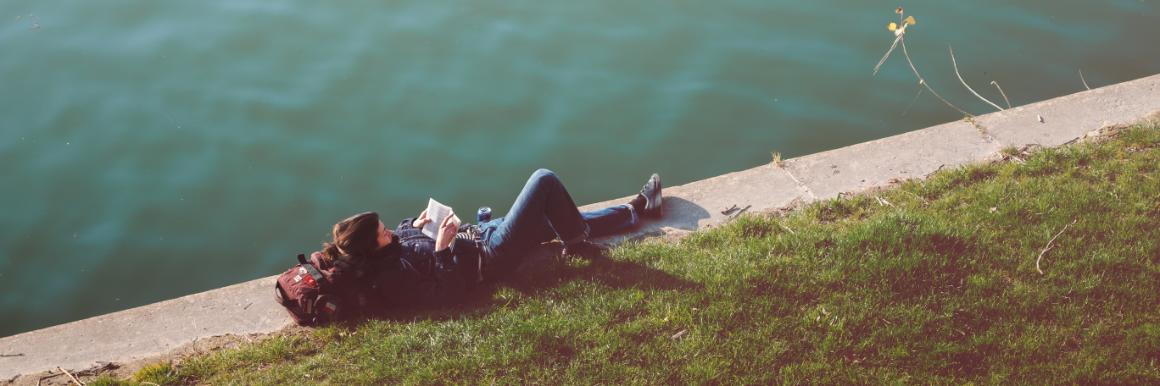 Young adult woman laying by the water reading a book image link to story