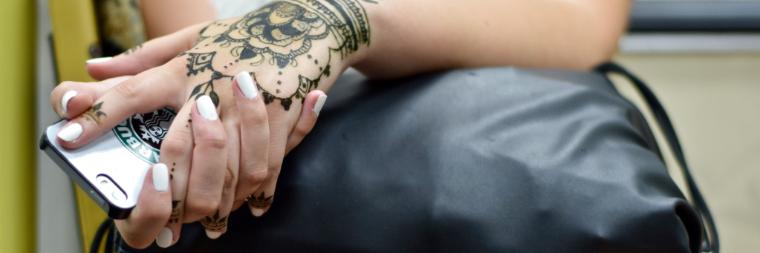 Woman sitting on public transportation with henna tattoos on hands holding iPhone image link to story