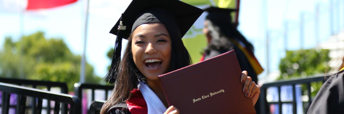 A Santa Clara graduate walking down the ramp holding her diploma at commencement  