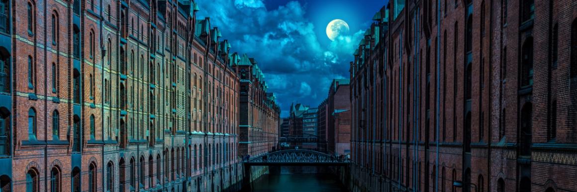 A full moon peaking out of clouds over city buildings with a river running through them and a bridge in the distance image link to story