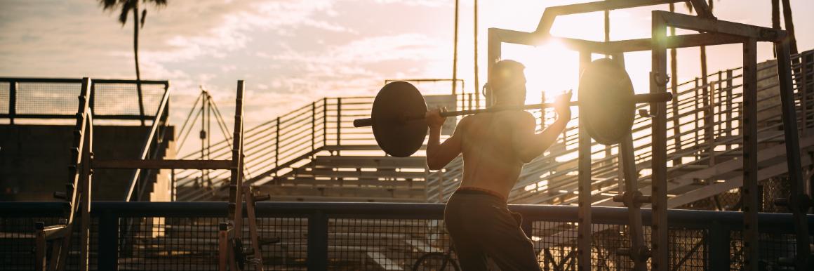 Man lifting weights at an outdoor beach-side gym at sunset