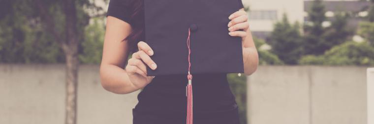 Woman in black dress holding a graduation cap in front of her