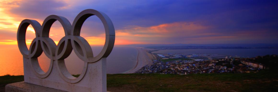 A statue of the Olympic rings on a hill above a coastal city at sunset