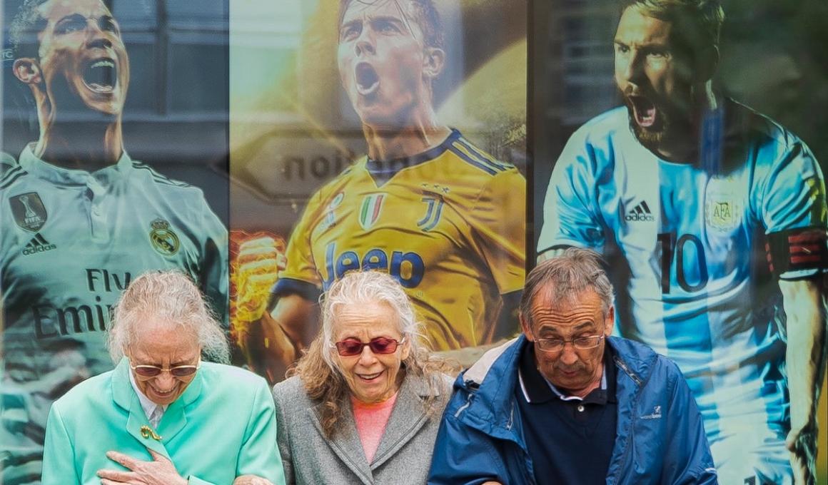 Photo of three elderly people walking in front of posters of soccer players.