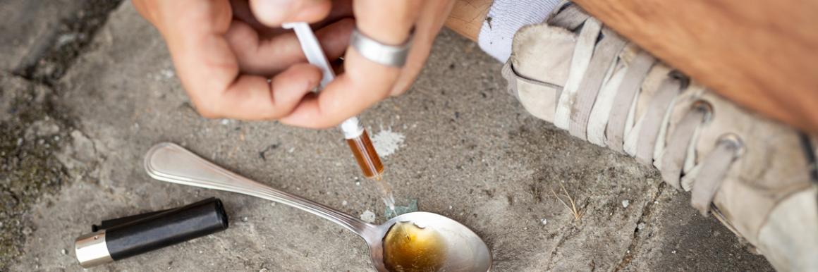 Photograph of drug addict preparing heroin in spoon, and needle.