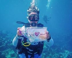 Female scuba diver holding sign that say I love SCU.