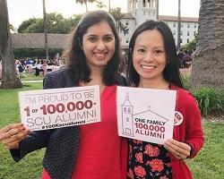 Two women posing with 100K SCU alumni signs.