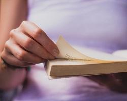 Photo of woman turning pages in a book.
