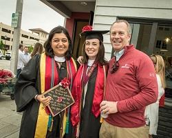 A dad stands with two female grads outside The Hut.