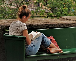 Woman sitting on a green park bench reading a book.