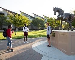 Three students standing physically distant on campus.