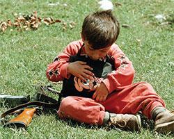 Young boy clutching Minnie Mouse bag and sitting next to a rifle.