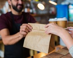 A man handing over a bag of takeout to a female customer.