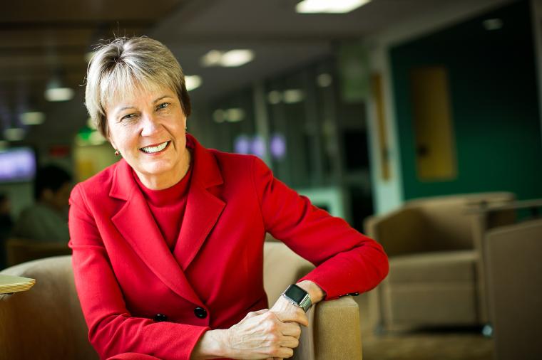 A person in a red jacket smiling in an office or lounge area. image link to story