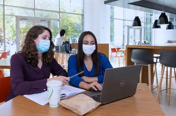 Two face masked female students working together inside Benson Center 