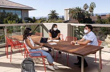 Three seated students meeting around a table on an SCU campus rooftop lounge 
