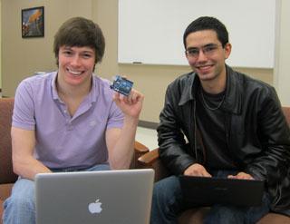 Two people smiling while seated indoors, one holding a small electronic device.