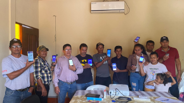 A group of ten people holding up their phones with the screen facing out as part of a small focus group with smallholder farmers testing a forecasting app.