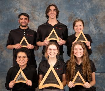 A group photo of 6 students holding a triangle shaped wooden award for winning second place in the Sustainability problem.