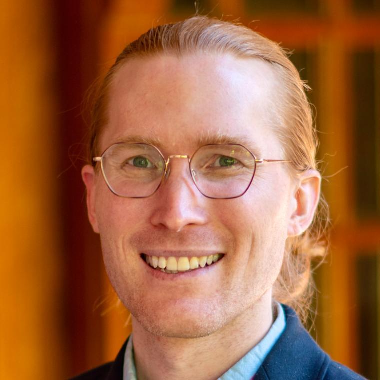 A smiling person with glasses looking to the right.