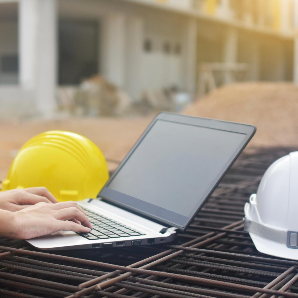 Hands typing on a laptop computer, with hard hats and construction site in the background image link to story