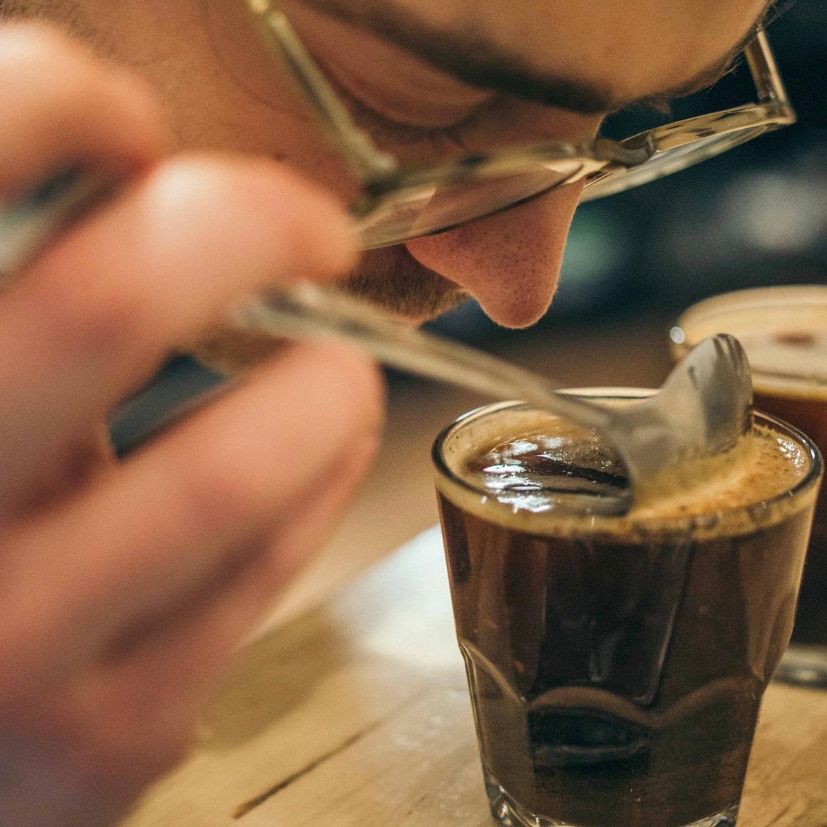 A man puts his nose over a glass of coffee to determine its aroma. image link to story