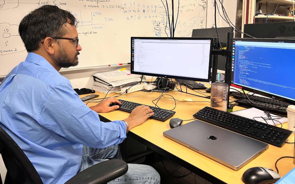 Male student wearing a blue shirt sitting at a desk while working on a computer