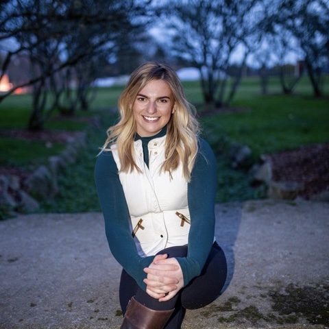 A person kneeling outdoors, smiling, with trees in the background.
