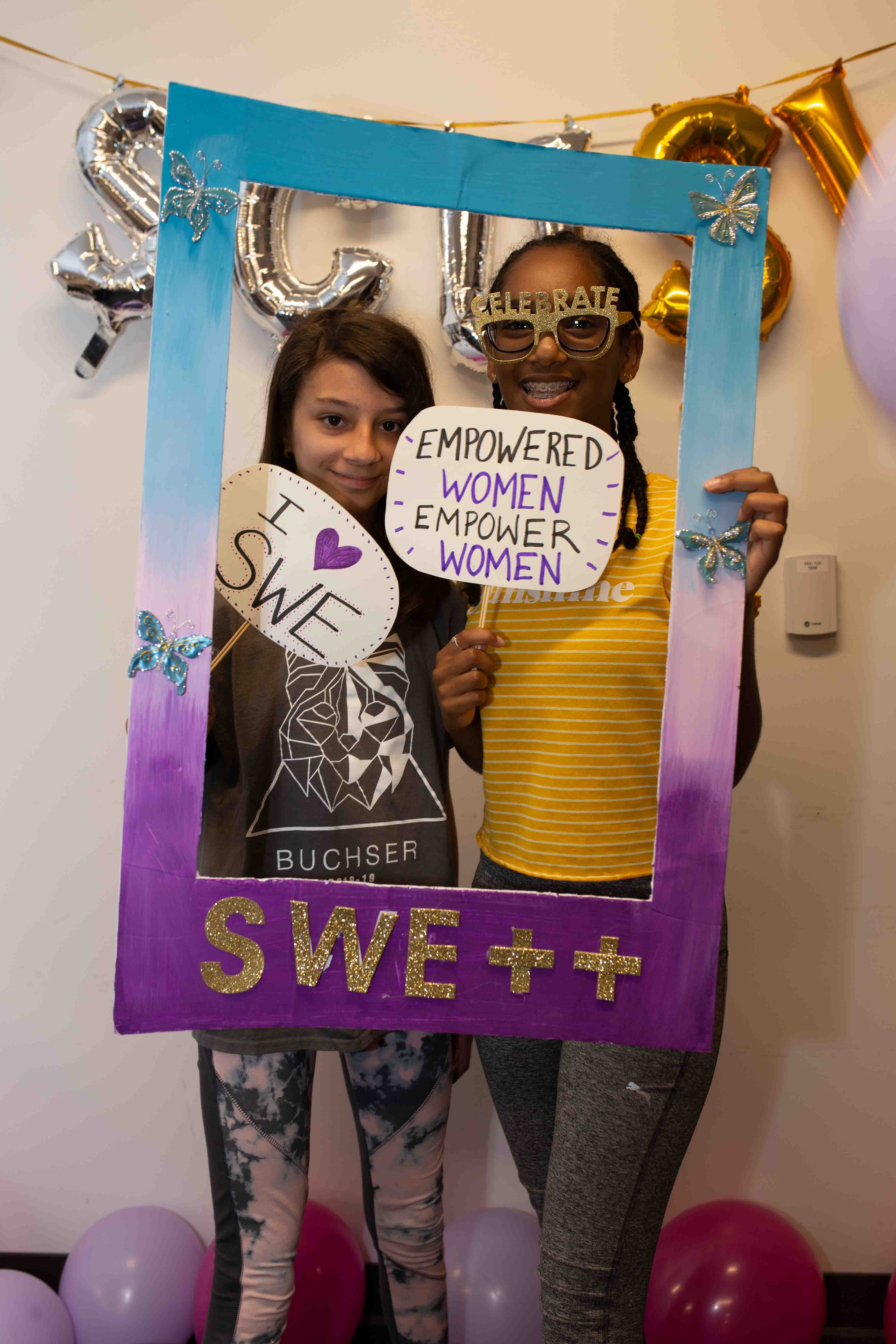 Two young diverse female students pose in a SWE++ frame during Girl Tech Day