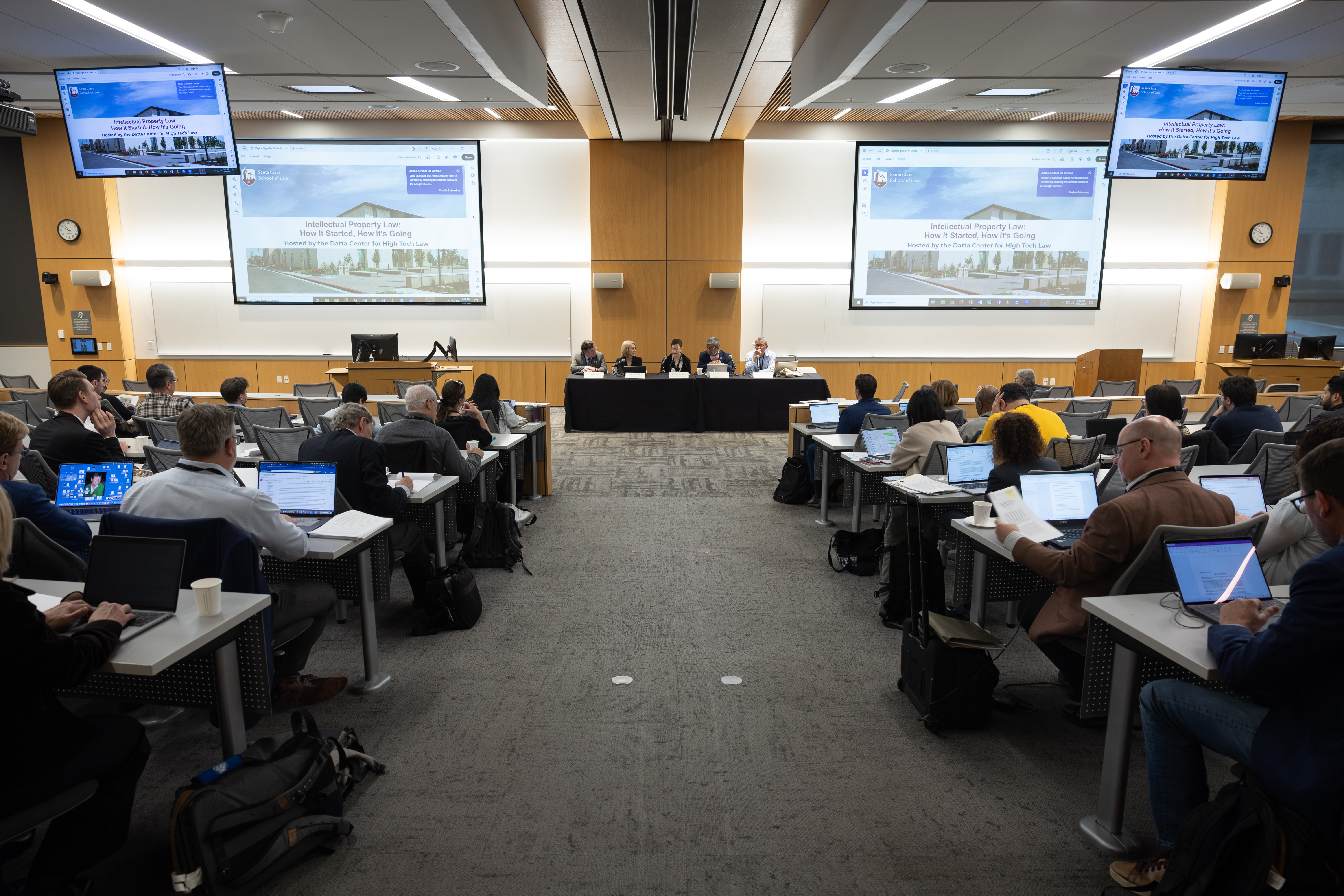 Big classroom with two screens and rows of tables with students at a conference