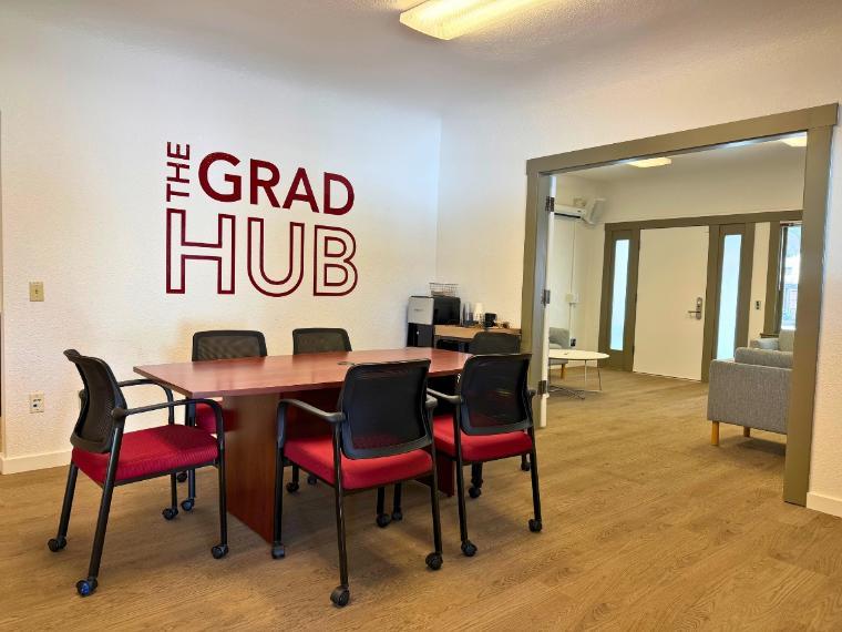 Grad Hub Dining Room with a long table and chairs around it, coffee station in the corner, and The Grad Hub vinyl decal on the wall 