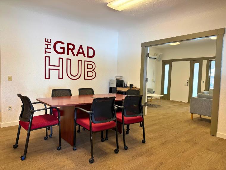 Grad Hub Dining Room with a long table and chairs around it, coffee station in the corner, and The Grad Hub vinyl decal on the wall 