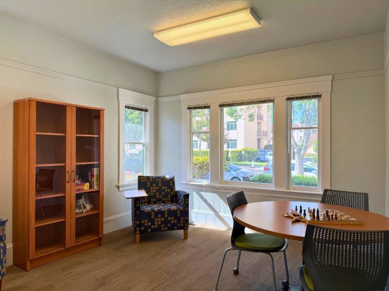 The grad hub library with a book shelf and a table to play chess on and a lounging chair in the corner 