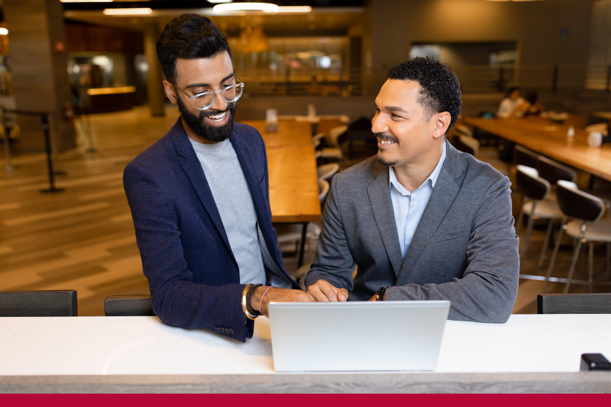 Two men in suits collaborating while viewing a laptop. 