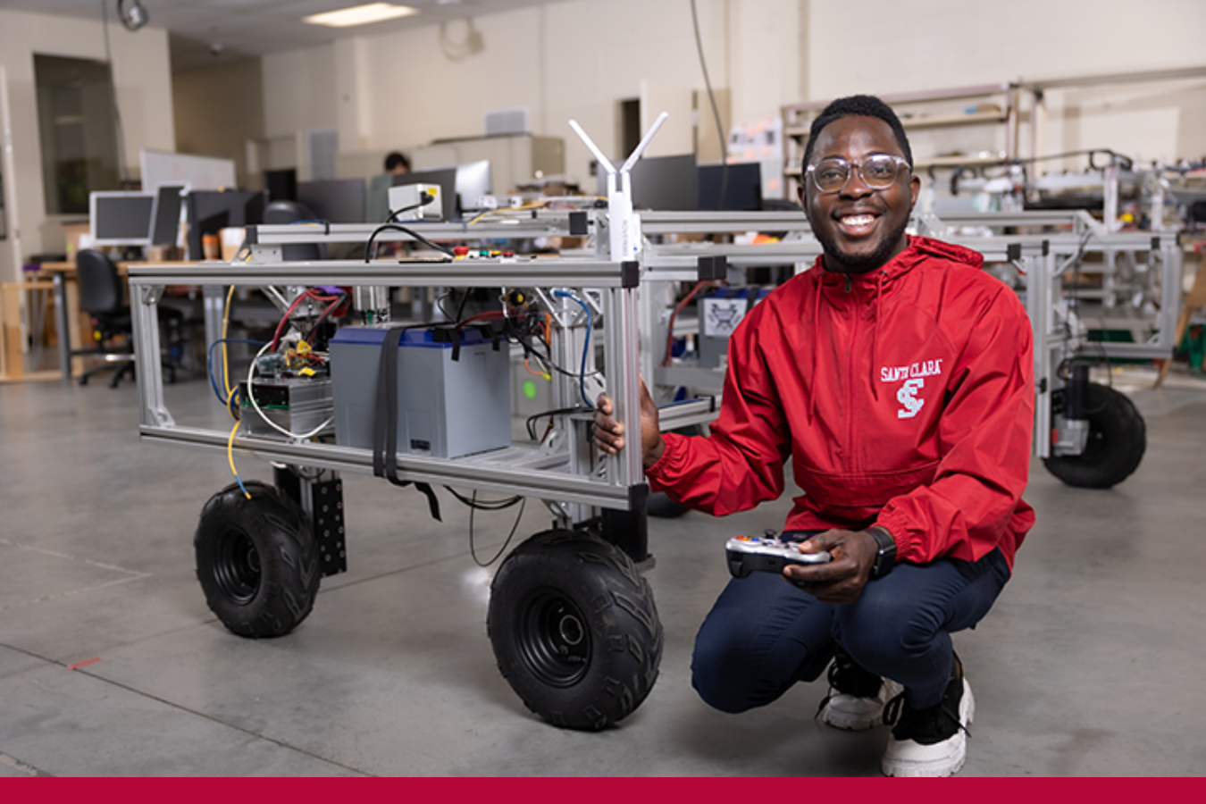 Man in red Santa Clara jacket next to a robot in the robotics lab 