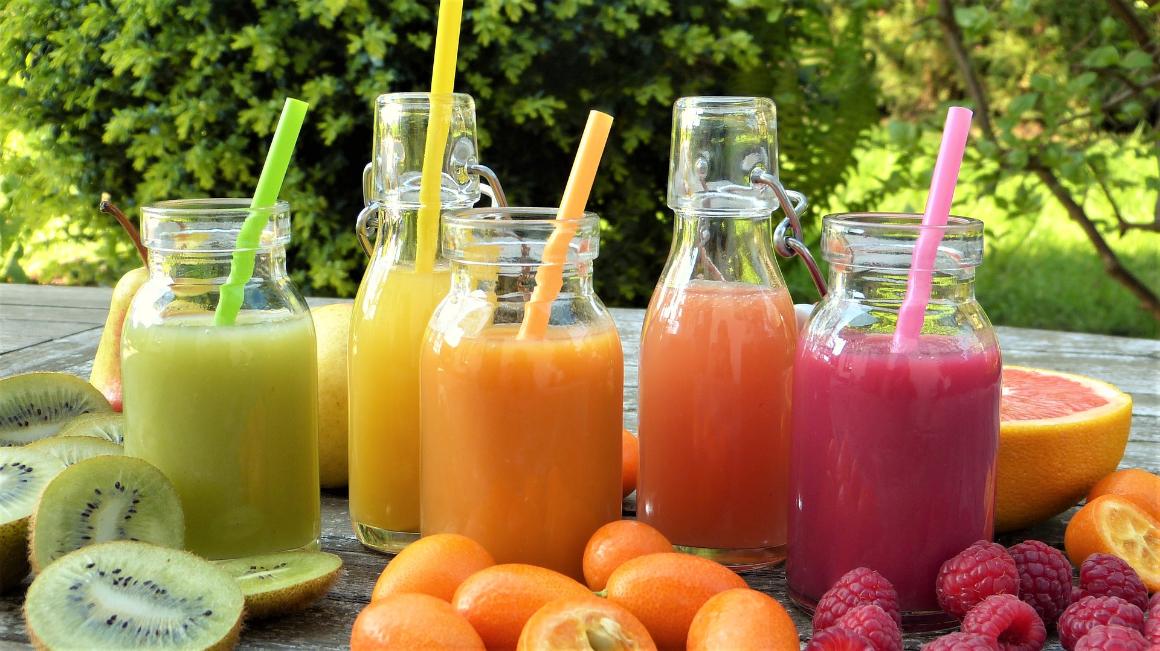 Five smoothies in jars with kiwi, orange, raspberries, and grapefruit on a table 