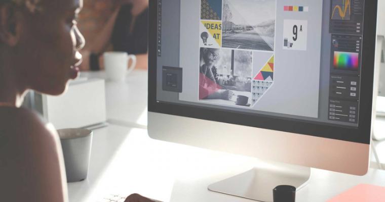 A woman works at her office desk with a pen, a notebook, and a laptop.