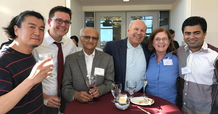 Business School faculty standing around a table smiling at the camera.