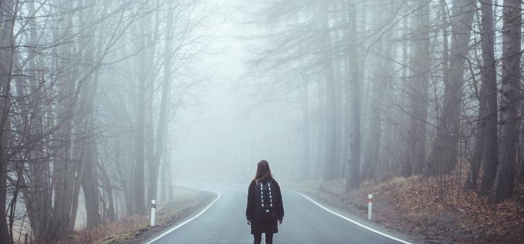 A woman walks in an empty road in a wooded area.