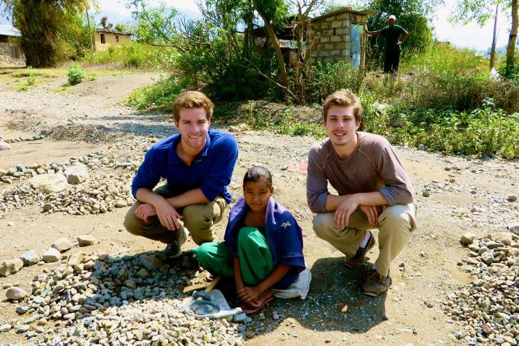 SCU mechanical engineering students with a child in Nepal, the students built a device to efficiently crush rocks, improving womens livelihoods.