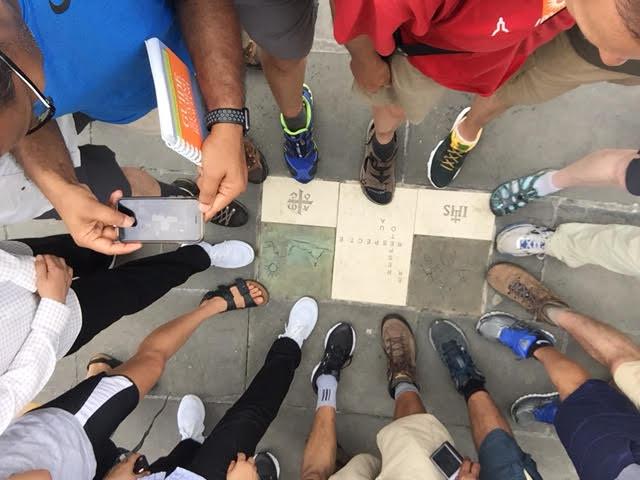 Students stand in a circle looking over religious tiles 