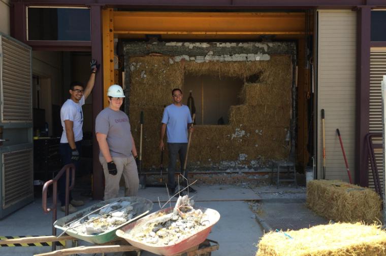 Three students stand in front of a strawbale wall in a testing bay