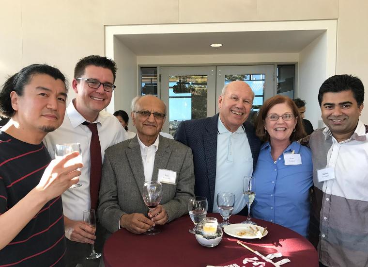Business School faculty standing around a table smiling at the camera. image link to story