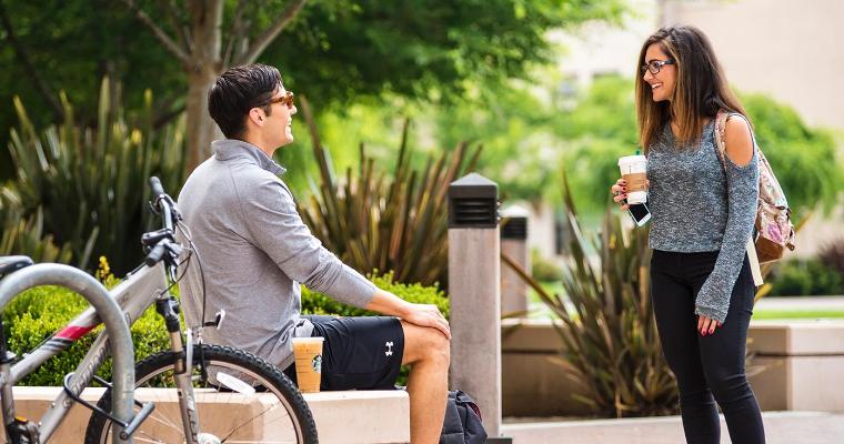 Two undergraduate students chat outside of the library on campus.